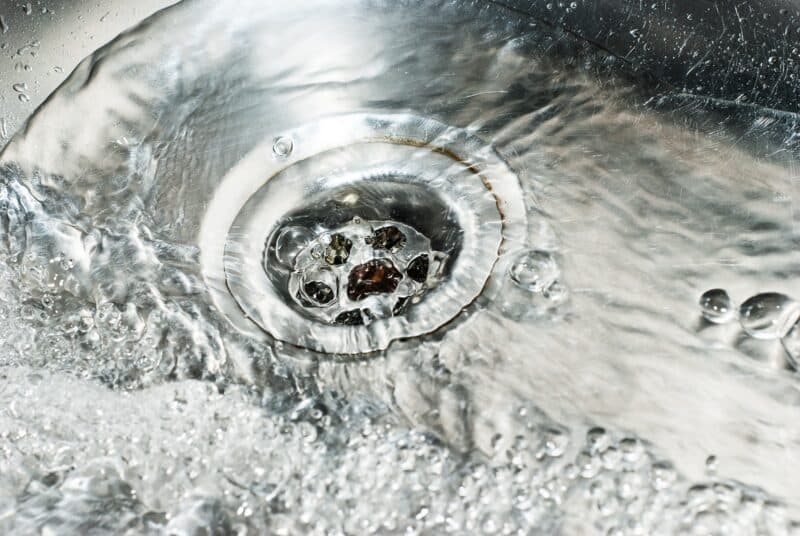 shiny metal sink and drain recently cleaned, with a lot of water flowing through the holes