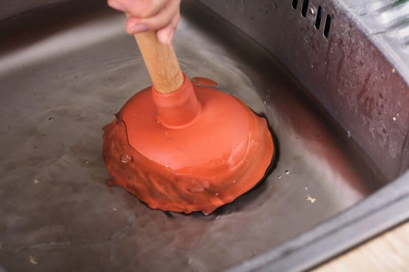 homeowner using an orange plunger over the clogged drain in a sink with standing water