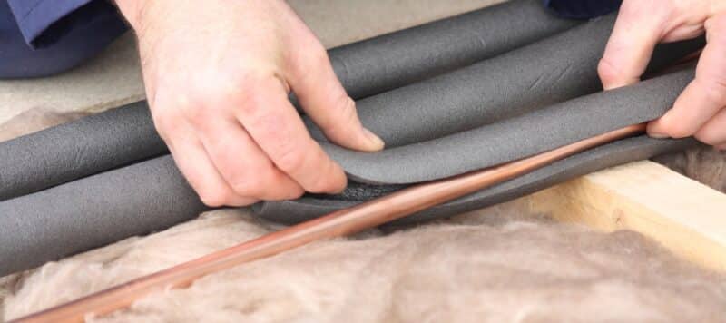 plumber placing gray foam isulation around thin copper pipes
