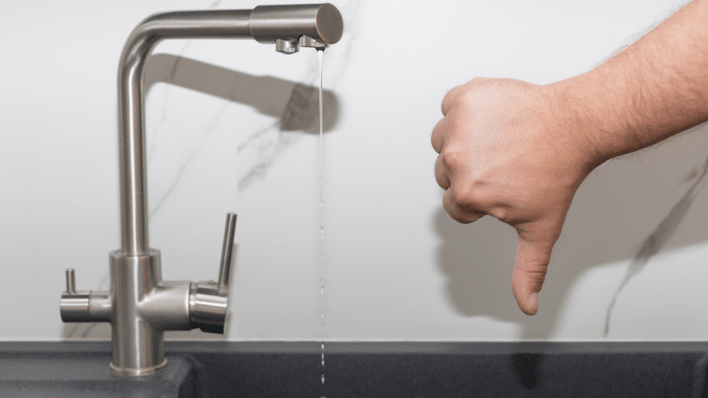 A sink faucet running a small stream and a hand making the thumbs down sign next to it