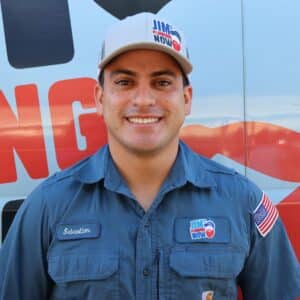 Jim's Plumbing Now team member wearing branded cap and company uniform, smiling in front of a company van