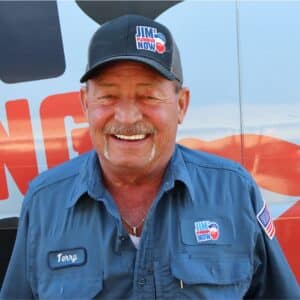Jim's Plumbing Now team member wearing branded cap and company uniform, smiling in front of a company van