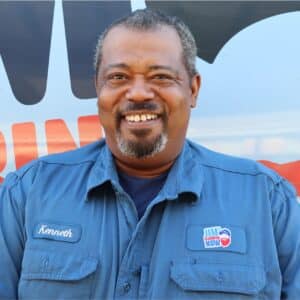 Jim's Plumbing Now team member wearing branded cap and company uniform, smiling in front of a company van