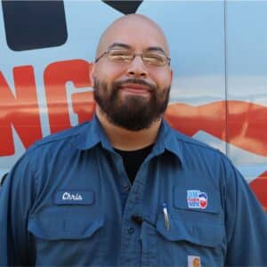 Jim's Plumbing Now team member wearing branded cap and company uniform, smiling in front of a company van