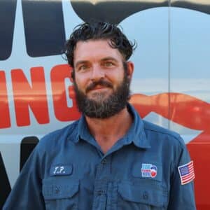 Jim's Plumbing Now team member wearing branded cap and company uniform, smiling in front of a company van