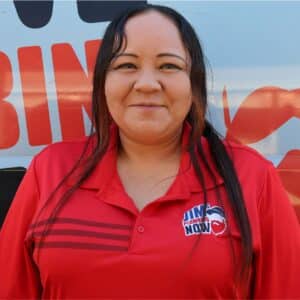 Jim's Plumbing Now team member wearing branded cap and company uniform, smiling in front of a company van