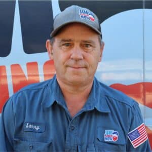 Jim's Plumbing Now team member wearing branded cap and company uniform, smiling in front of a company van