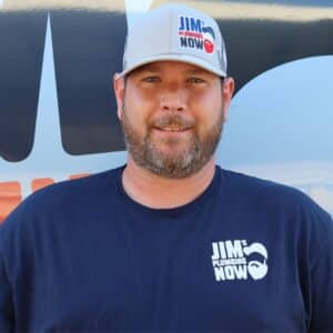 Jim's Plumbing Now team member wearing branded cap and company uniform, smiling in front of a company van