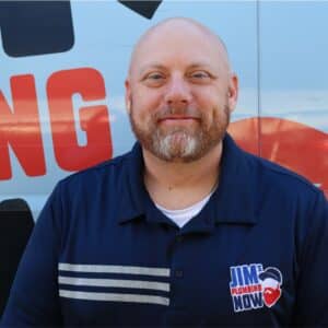 Jim's Plumbing Now team member wearing branded cap and company uniform, smiling in front of a company van