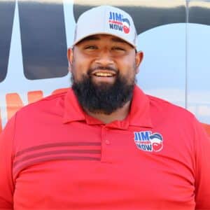 Jim's Plumbing Now team member wearing a red polo and branded cap, smiling in front of a company van