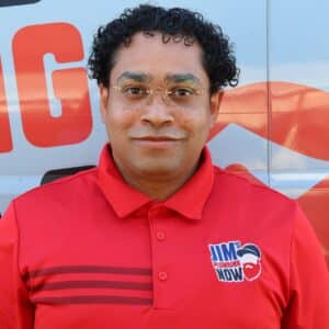 Jim's Plumbing Now team member wearing branded cap and company uniform, smiling in front of a company van