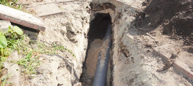 A partially buried pipe in a trench, surrounded by soil and patches of grass
