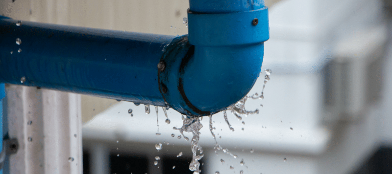 Leaking blue pipe with water spraying out from a damaged joint